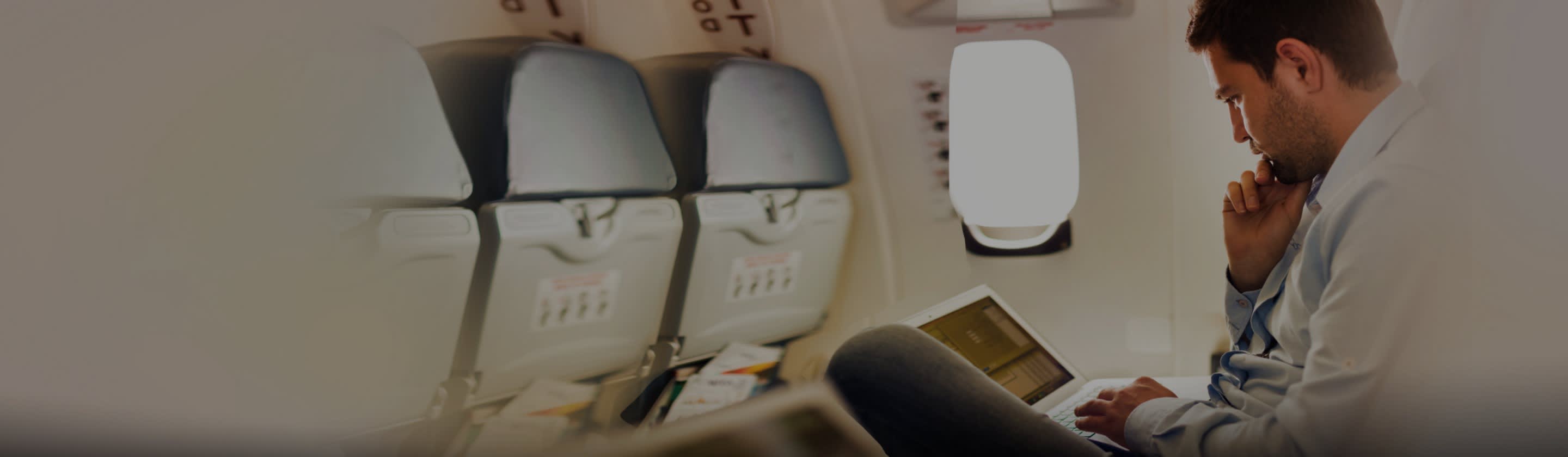 Moški na letalu uporablja prenosni računalnik. 