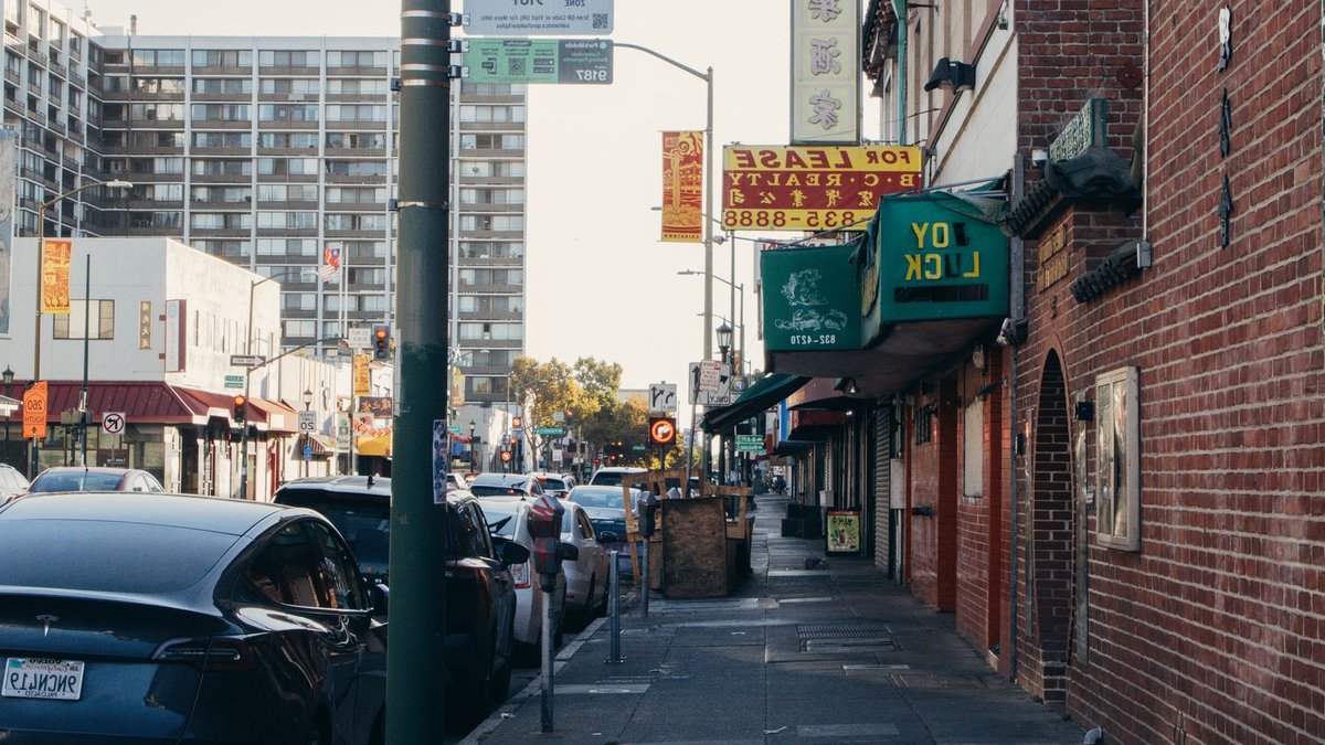 One in five drivers unaware of EV leasing option A street view in Oakland's Chinatown featuring shops, parked cars, and a clear sky.