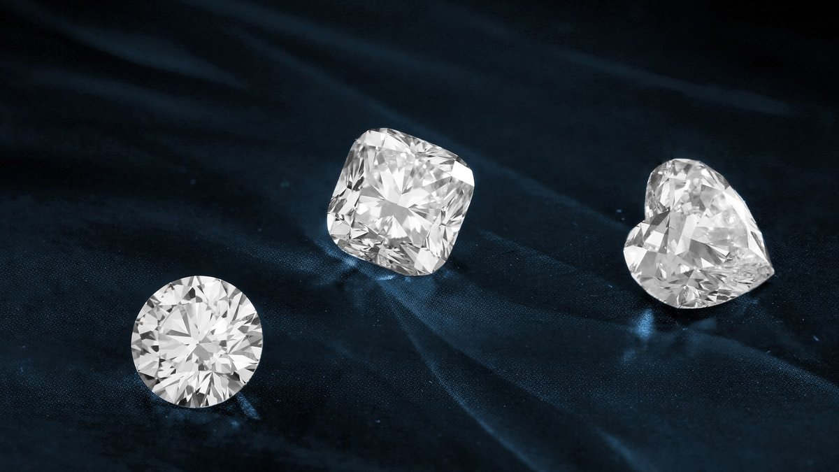 Three exquisite diamonds featuring heart, cushion, and round cuts displayed on dark fabric.