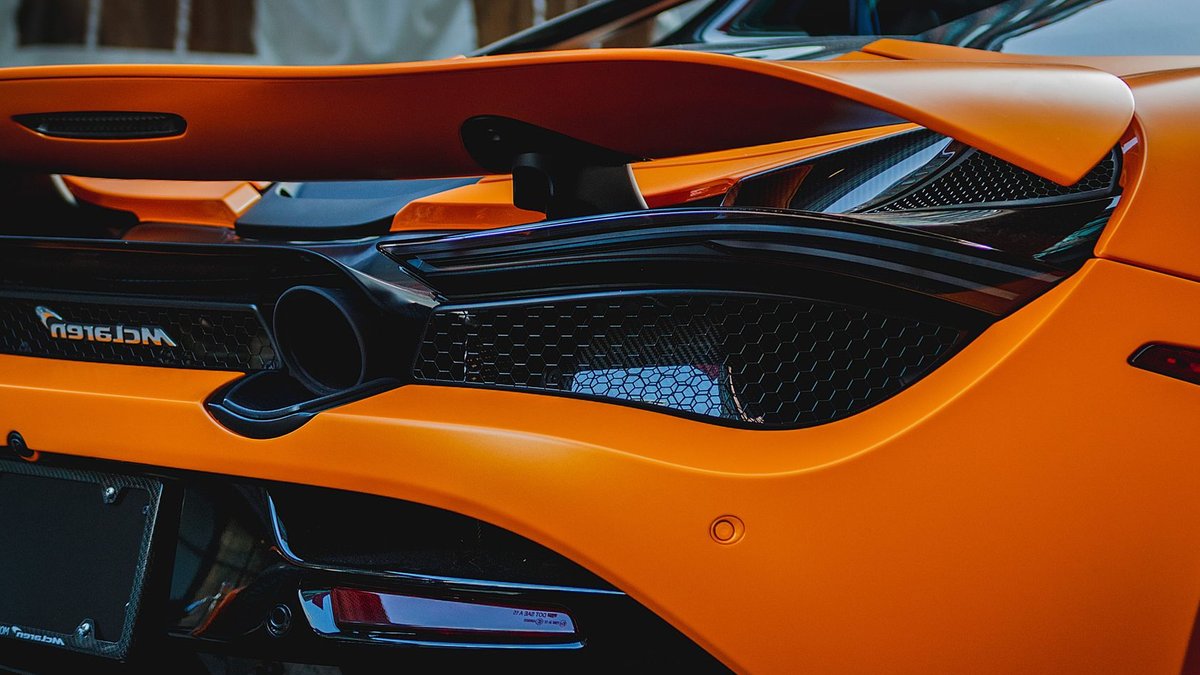 McLaren Confirms First SUV Alongside New Logo Close-up of a luxury orange McLaren supercar with visible spoiler and tail lights.