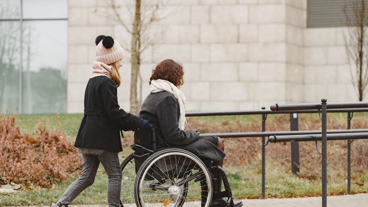 Closing Stroke Prevention Gaps in Underserved Communities A young girl helps a woman in a wheelchair on a sidewalk, showing care and support.