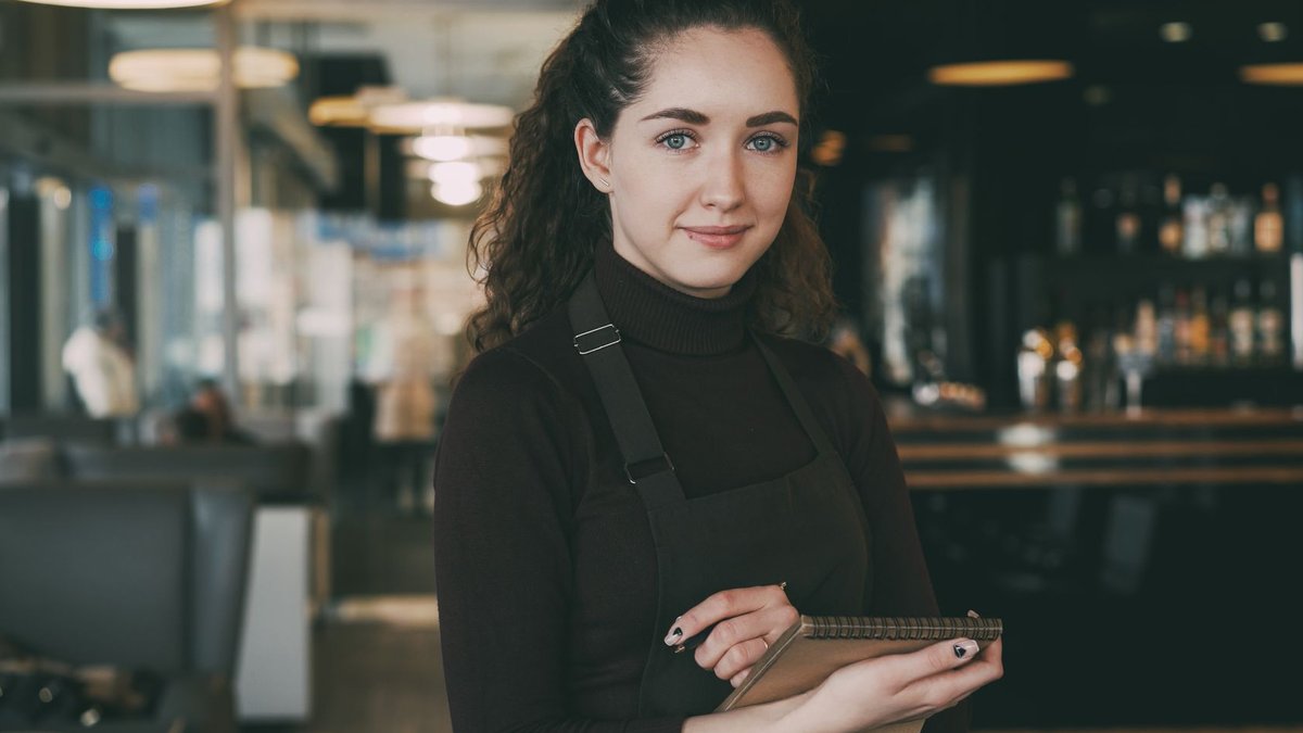 Friendly waitress holding a notepad, ready to take orders in a modern cafe setting.