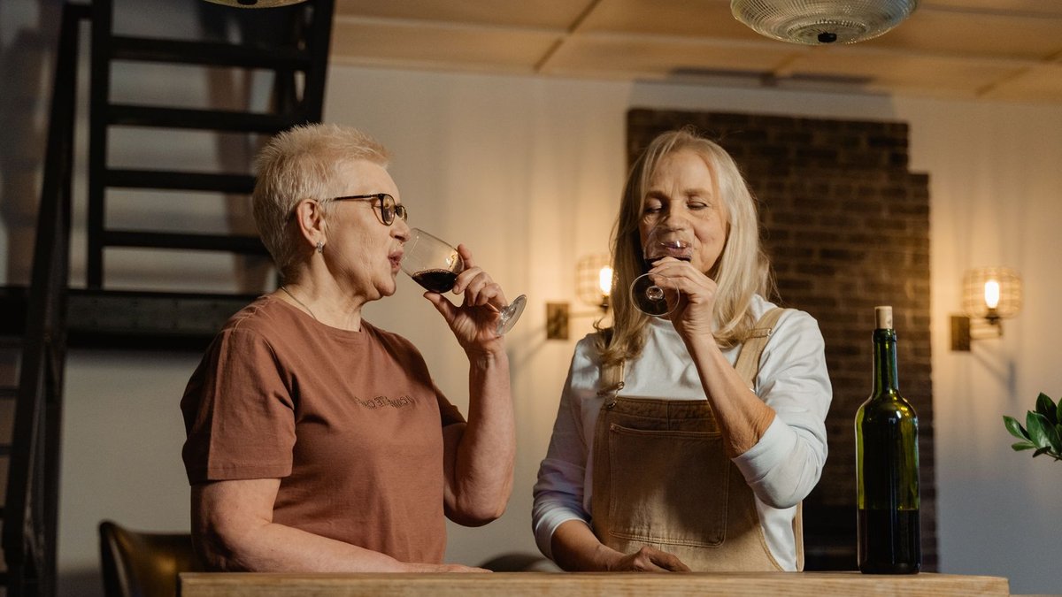 Government defends super's retirement-only purpose amid housing debate Two senior women savoring red wine in a cozy indoor setting, sharing a joyful moment.