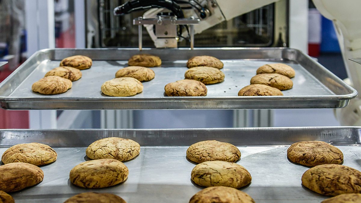 Robot arm preparing cookies for the oven in production line factory, industrial food production.