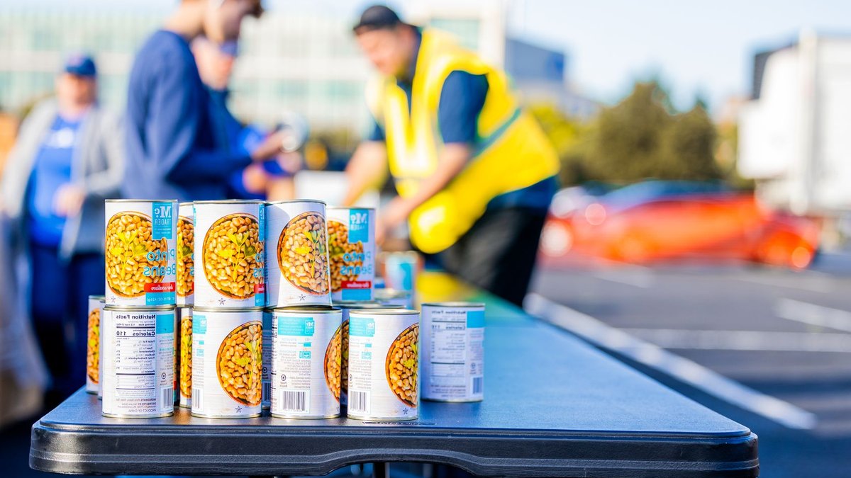 Tesco backs £20m food fund to boost UK affordability Canned goods displayed on a table during a community outdoor food distribution event.