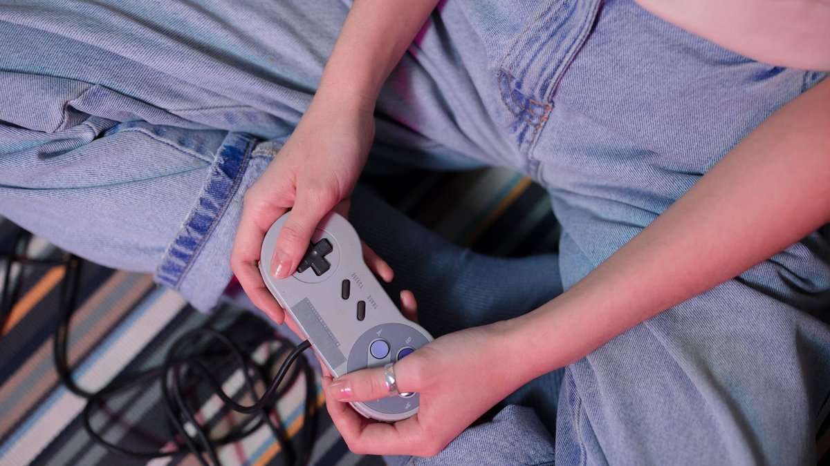 Gaming evolves from shared fun to monetized obsession Close-up of a young woman holding a retro game controller indoors, enjoying gaming.