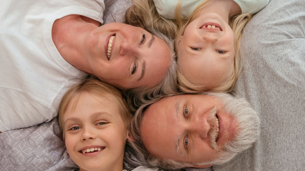 Family Doctors Weigh Multiple Factors Before Hearing Referrals A joyful multigenerational family lying down and smiling together, displaying warmth and affection.