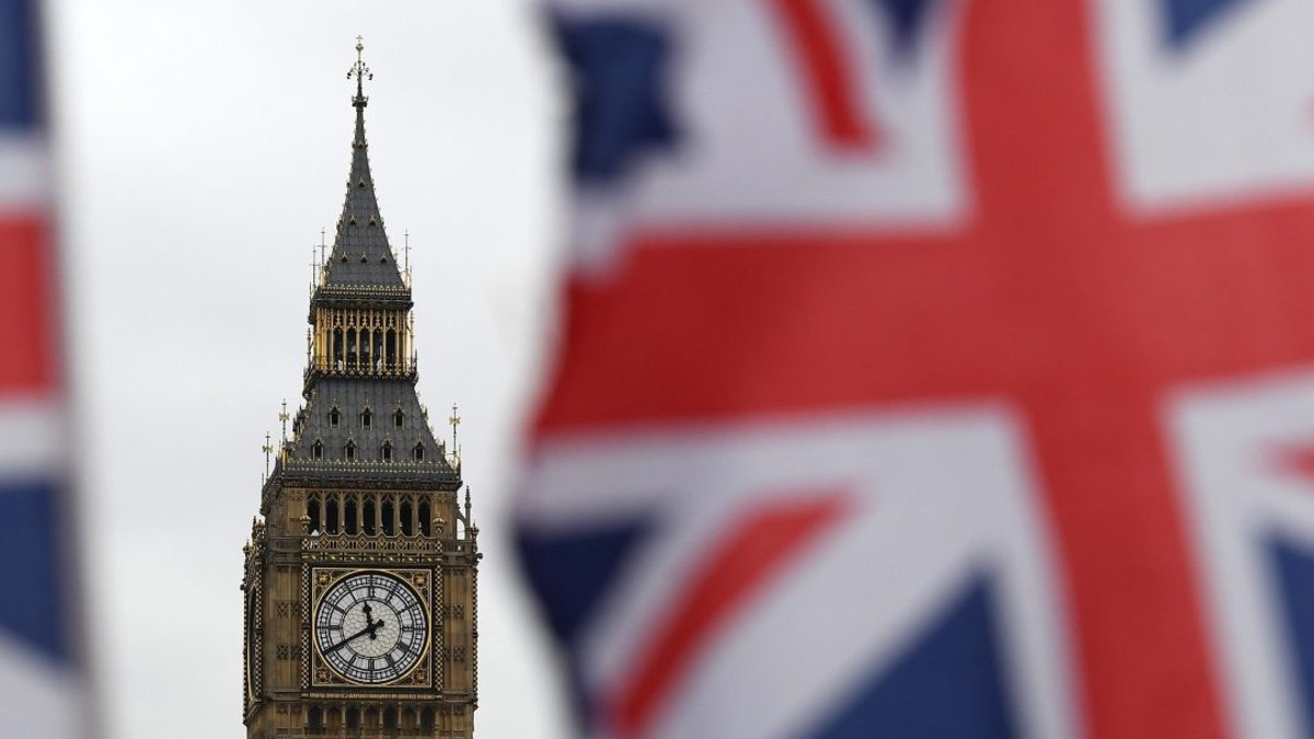 Big Ben clock tower with the British Union Jack flag blurred in the foreground, representing UK parliament.
