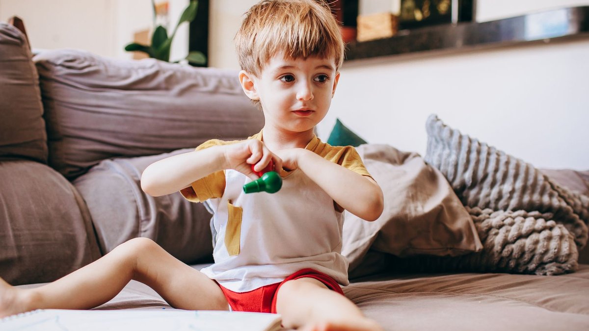 Children's Day highlights five workplace improvement lessons A child sits on a couch at home, playfully holding a toy and surrounded by a cozy living room setting.