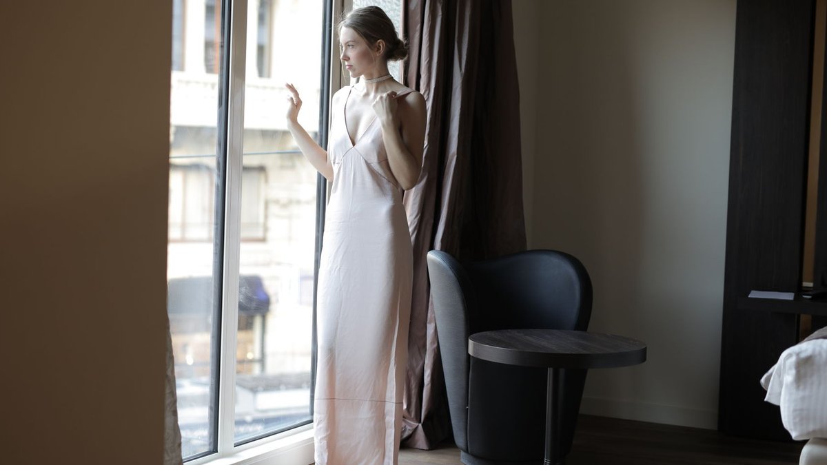 New VIP ROOM opens in Milan A woman in a long dress stands by a window in a modern hotel room, creating a serene indoor scene.