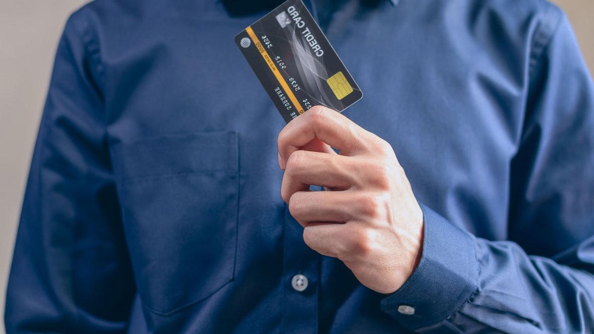 Close-up of a man in a blue shirt holding a credit card, symbolizing finance and security.