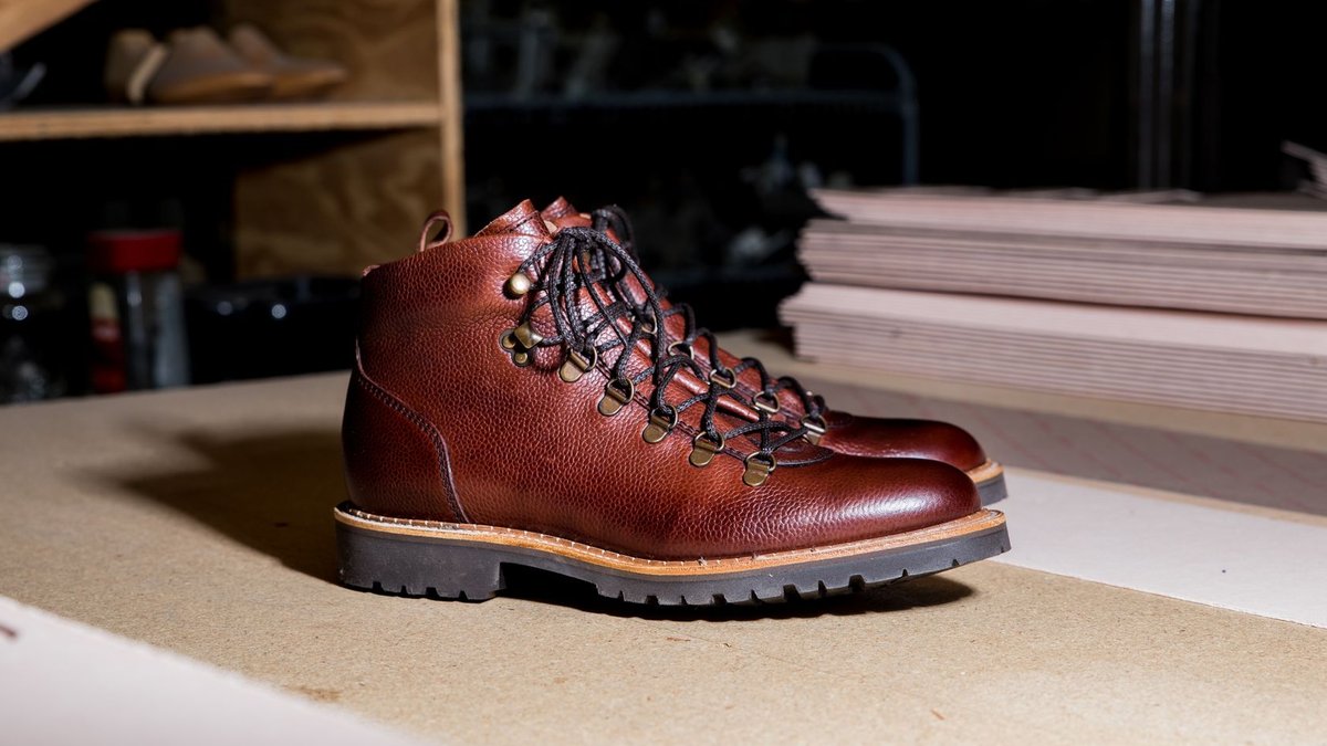 Close-up of brown leather boots with a rugged sole on a workshop table, showcasing craftsmanship.