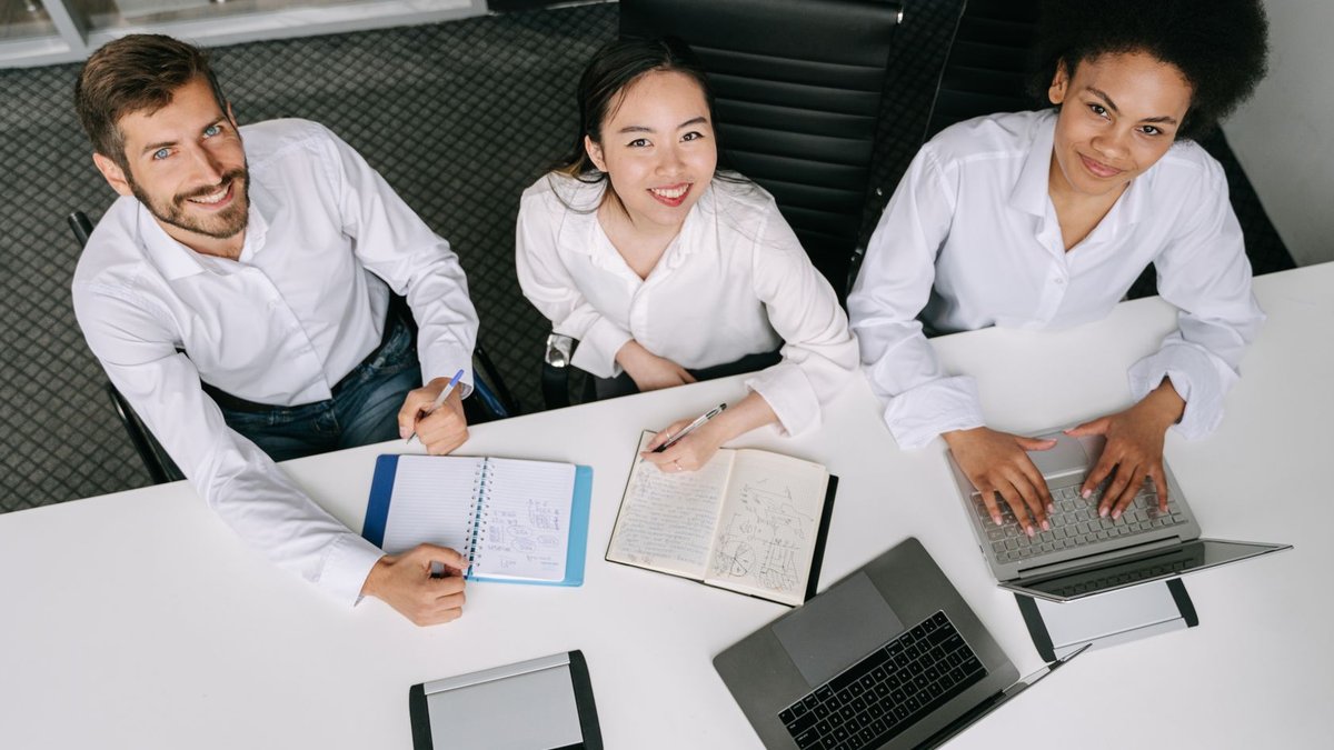 Companies adapt flexible tech to keep skilled workers engaged A diverse group of professionals collaborating during an office meeting, using laptops and notebooks.