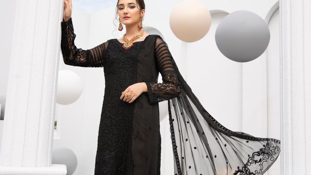 Interior Designer Transforms Rented Living Room With Black And Gold Elegant woman posing in a traditional black dress with modern earrings and makeup against a contemporary backdrop.