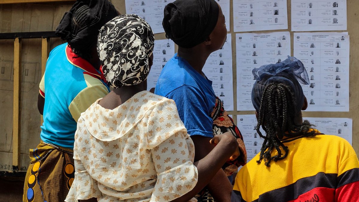 Google's AI Watermark Tool Faces Nigeria Election Test A group of women reading election lists posted on a wall outdoors during the day.