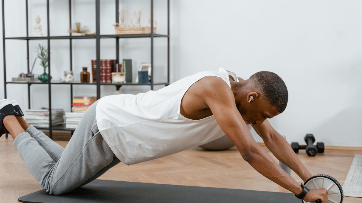 Young man working out with an ab roller on a yoga mat to improve core strength.