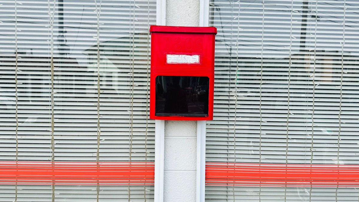 India Offers Post Office Savings Schemes Red post box on a street wall with striped window blinds behind. Minimalist urban style.