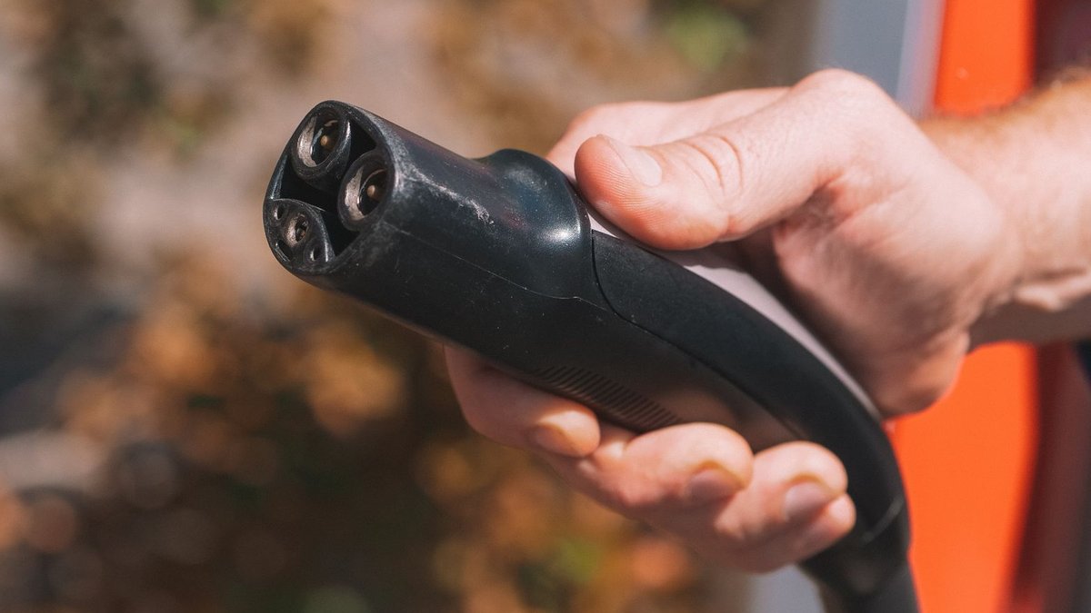 Hand holding an electric vehicle charging plug, symbolizing clean energy and innovation.