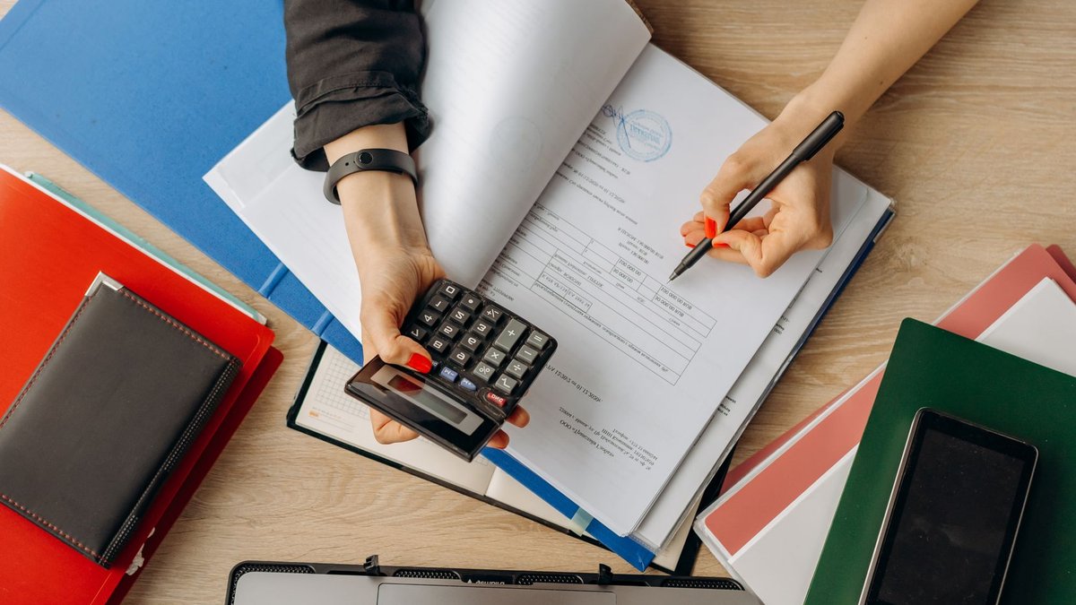 India’s PMJDY scheme expands financial access for millions Accountant analyzing financial documents with a calculator on a desk, highlighting business tasks.
