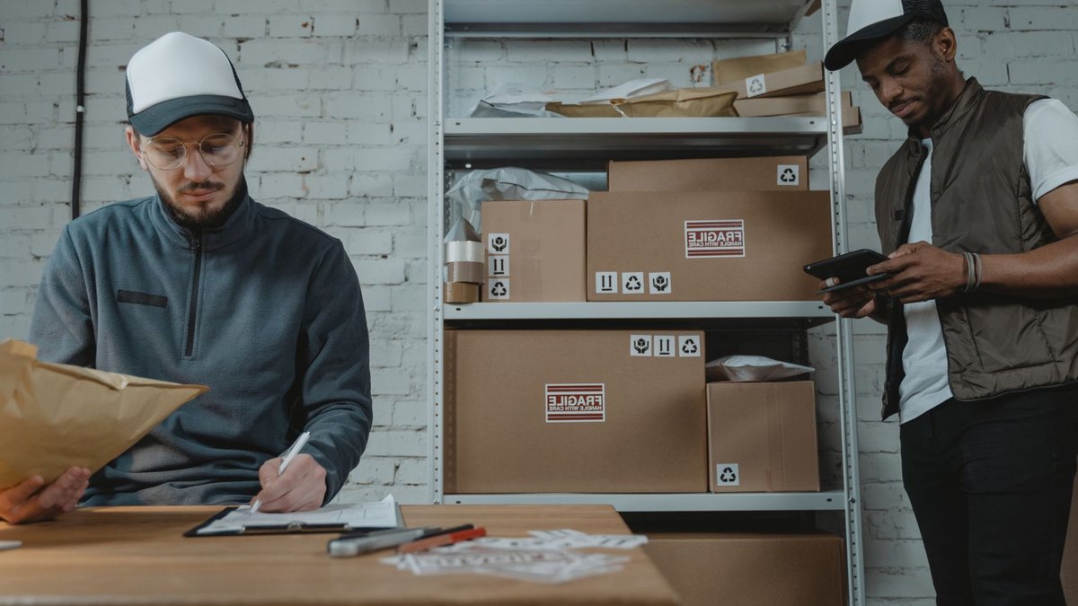 New EU rules add fees to small orders Warehouse employees organizing shipments with packages and documentation in a brick-walled workspace.