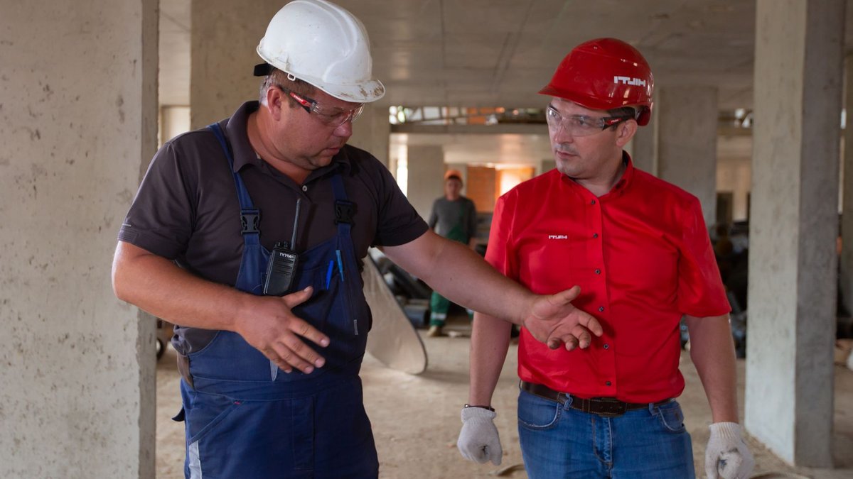 Two construction workers in safety gear discussing plans at a construction site.