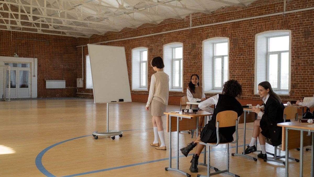 Students in school uniforms engaged in a lesson with a teacher in a spacious classroom.