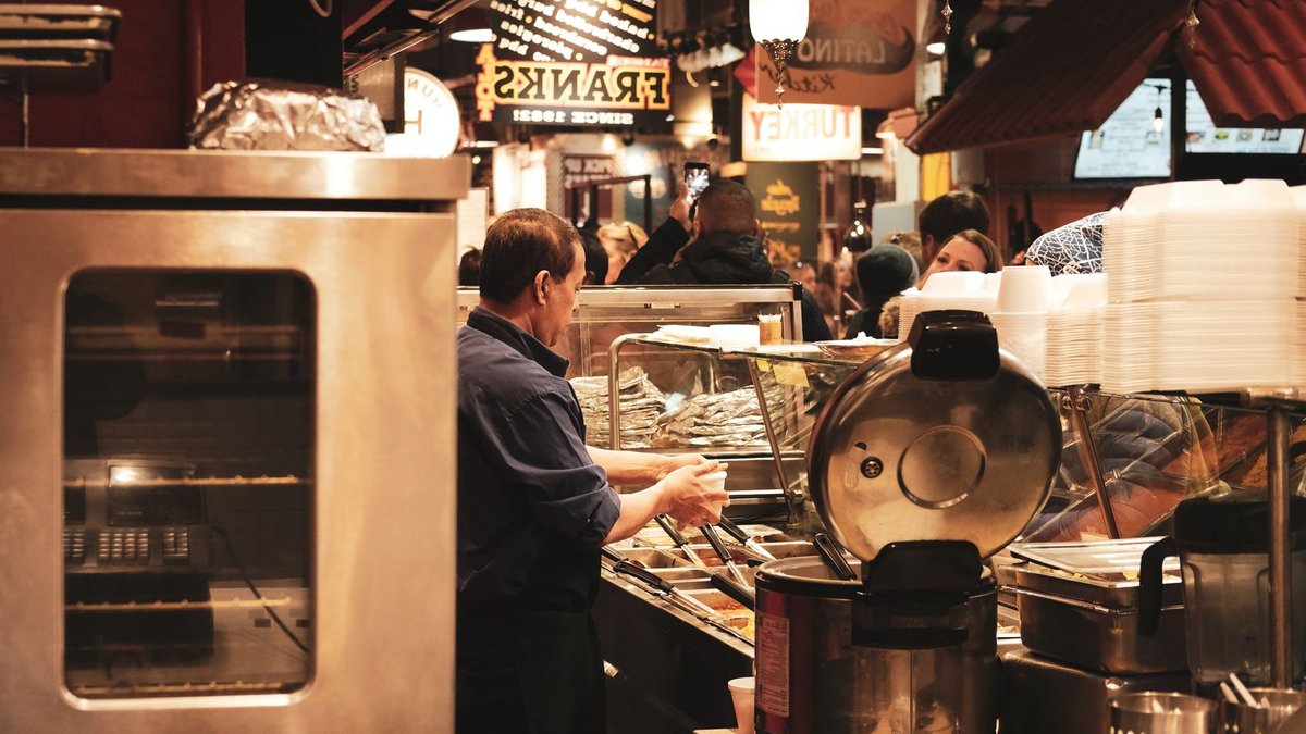 A busy food hall with a man preparing food, showcasing bustling market activity.