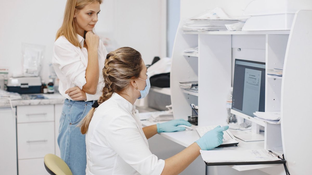 Two female healthcare workers in a clinical office, reviewing diagnostic results on a computer screen.