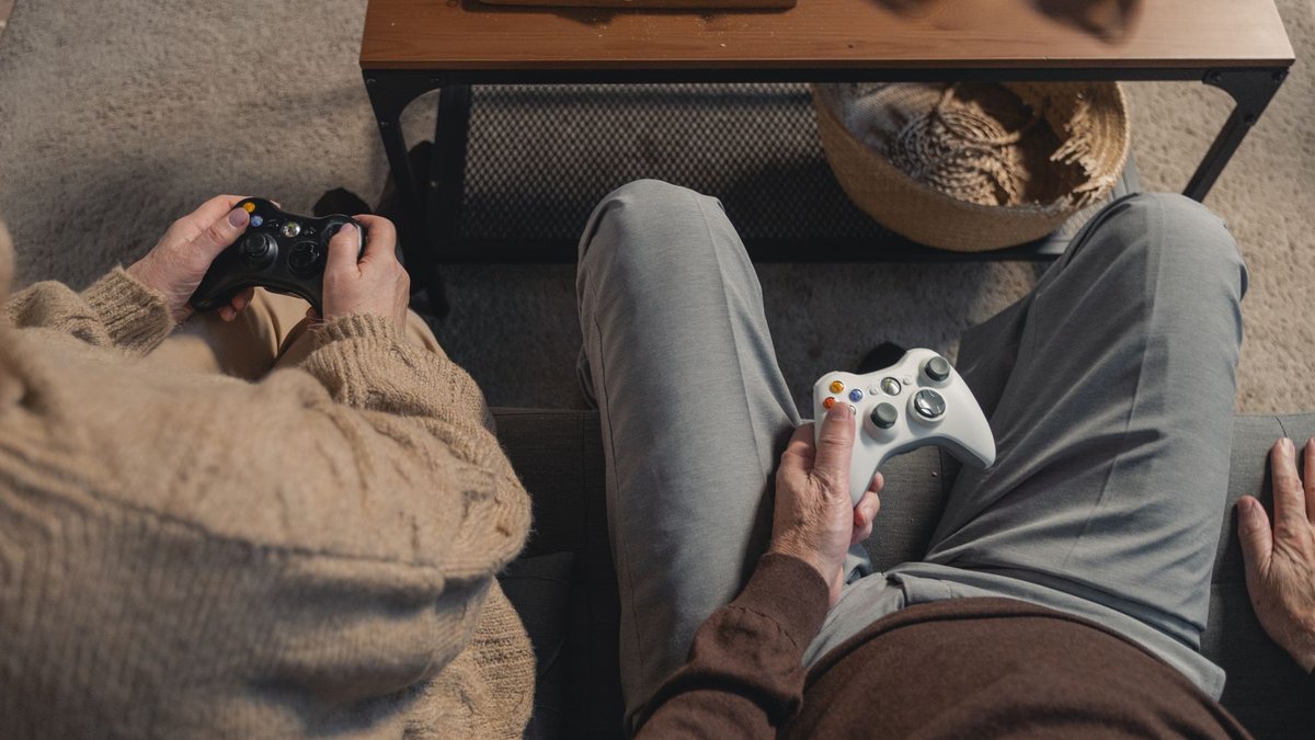 Elderly couple playing video games on the sofa, enjoying leisure time with a console.