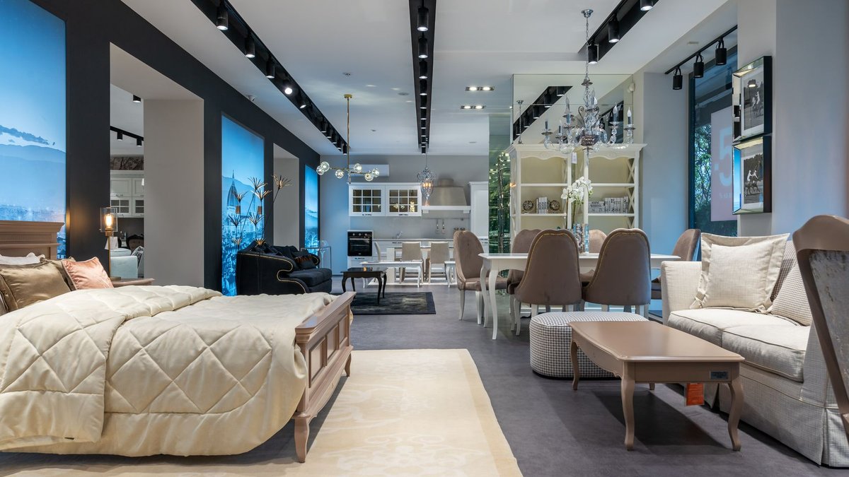 Interior of spacious furniture store with classic styled bed with coverlet and cushions placed in front of soft couch and din