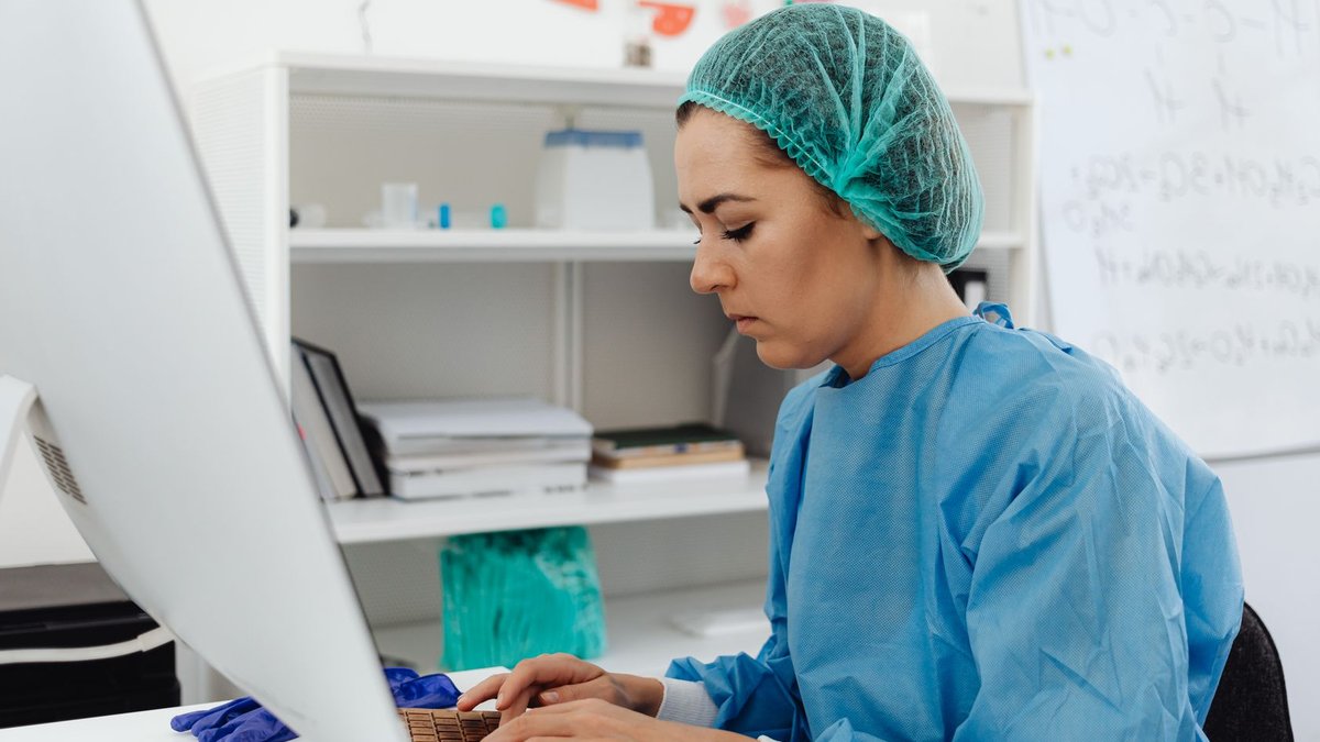 A female healthcare professional in scrub suit working on a computer in a laboratory setting.