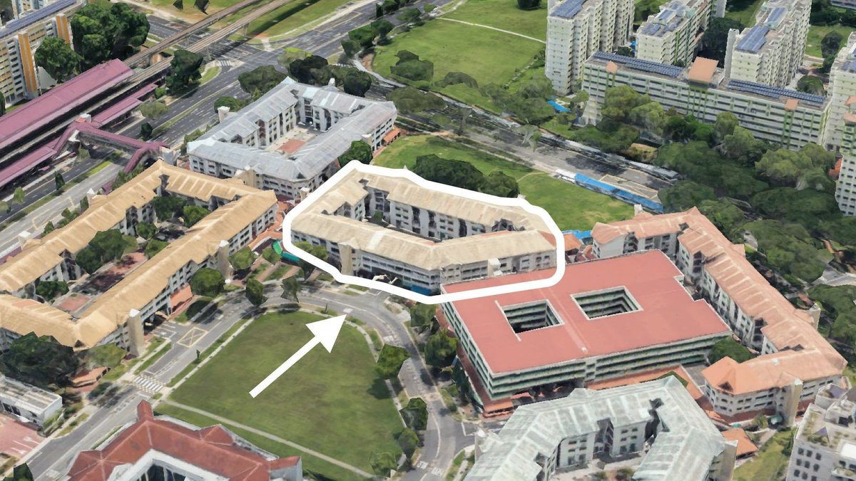 Cluster of low-rise housing blocks outlined beside a curved road and large green field with high-rise blocks nearby.