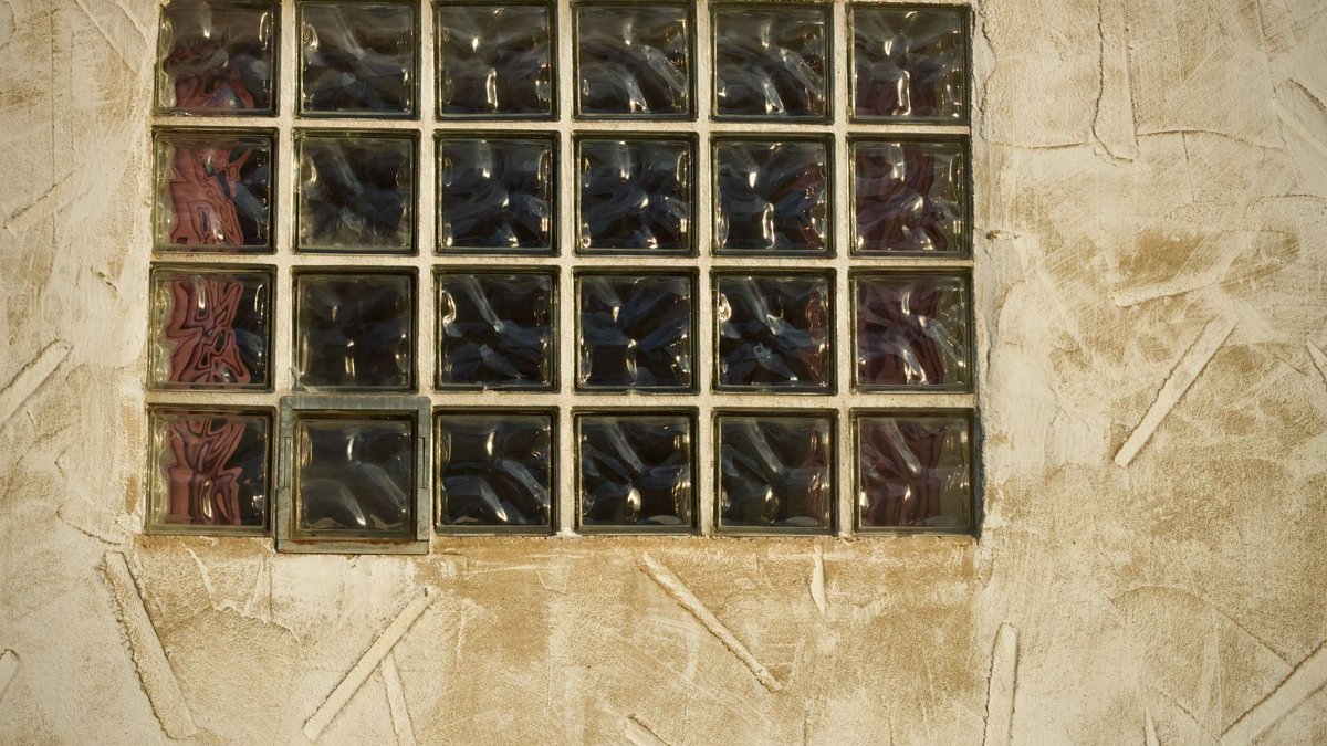 Close-up of a textured glass block window in a beige stucco wall, showcasing artistic design.