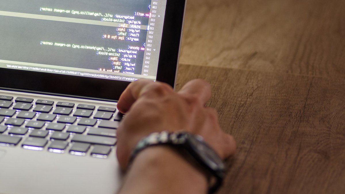 A developer's hand interacting with code on a laptop screen in a workspace setting.