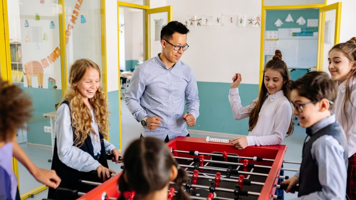 A joyful classroom scene with students and teacher enjoying a game of foosball together.