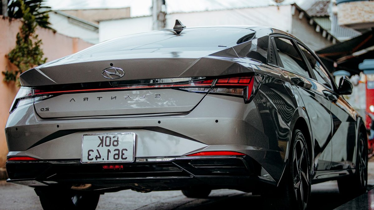 Performance sedans clash in opposing design philosophies Sleek silver Hyundai Elantra parked on a wet urban street with license plate visible.