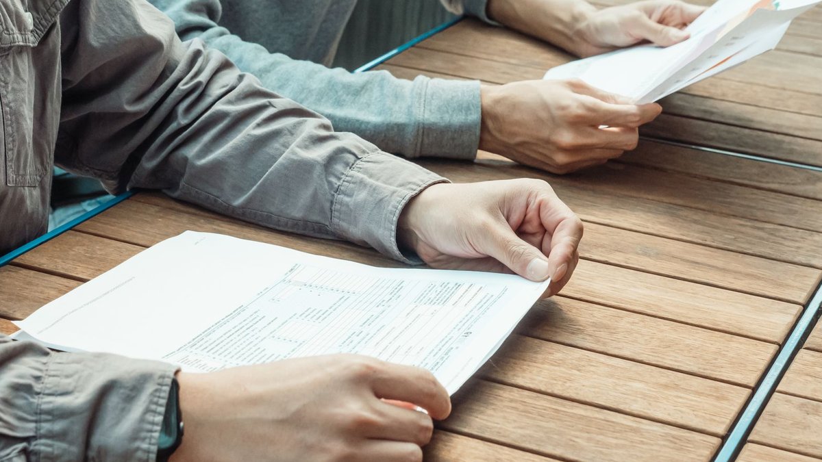 Two people reviewing business documents at an outdoor table, focused on paperwork.