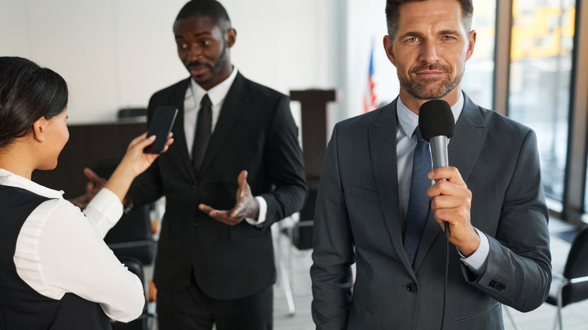 A journalist interviews a businessman in a conference room, capturing a professional and political setting.