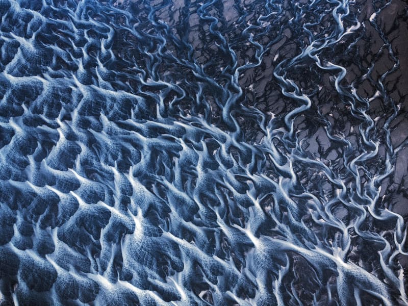 Aerial view of braided glacial rivers on black sand.