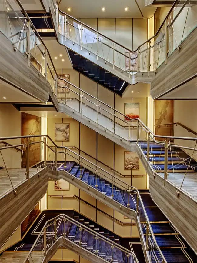 A striking multi-story atrium aboard a luxury cruise ship featuring contemporary staircases