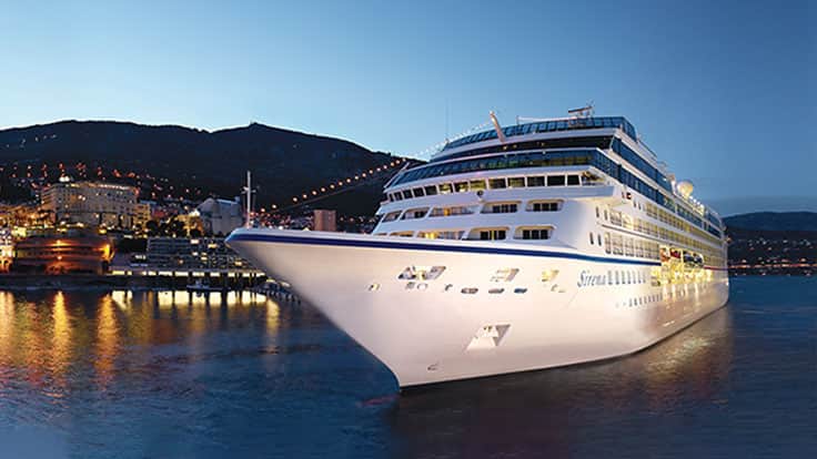 A luxurious multi-deck cruise ship illuminated at dusk, moored in a scenic Mediterranean