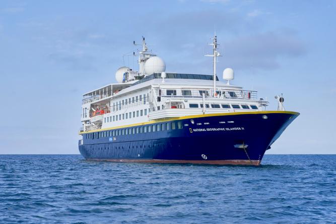 A modern expedition cruise ship with distinctive blue hull and white superstructure sailing on calm blue waters. The vessel features multiple decks, communication equipment on top, and appears to be a luxury expedition cruiser designed for exploration and discovery voyages.
