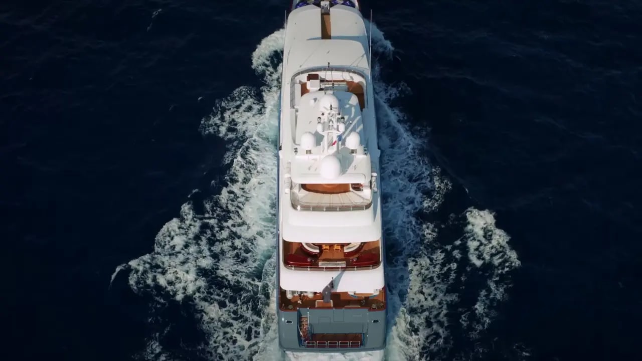 An overhead aerial view of a multi-deck white luxury motor yacht cutting through deep blue ocean