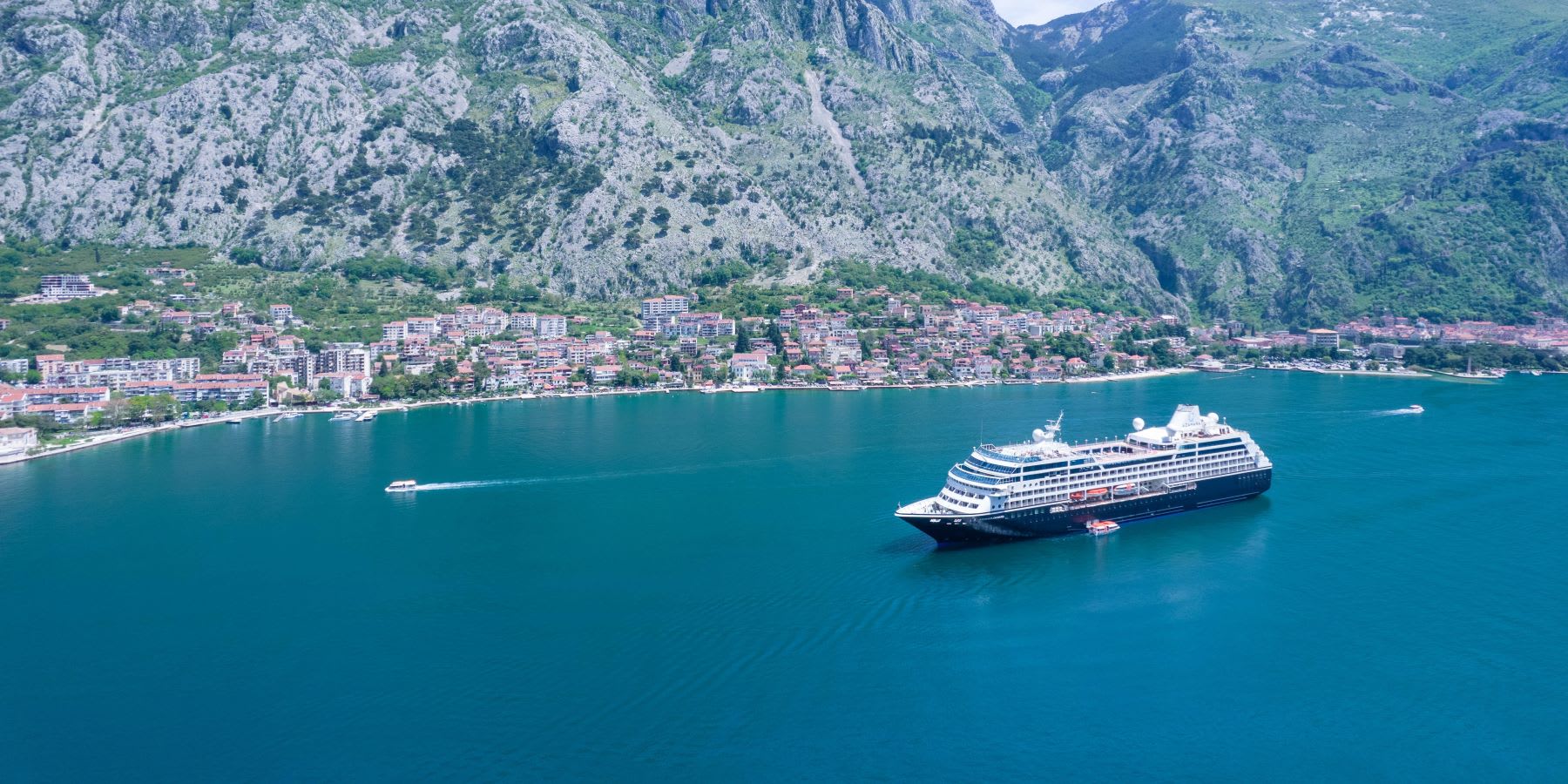 A modern luxury cruise ship anchors in crystal-clear turquoise waters of a dramatic Adriatic fjord