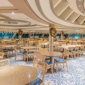 A spacious and elegantly designed lido dining area aboard a cruise ship, featuring multiple round