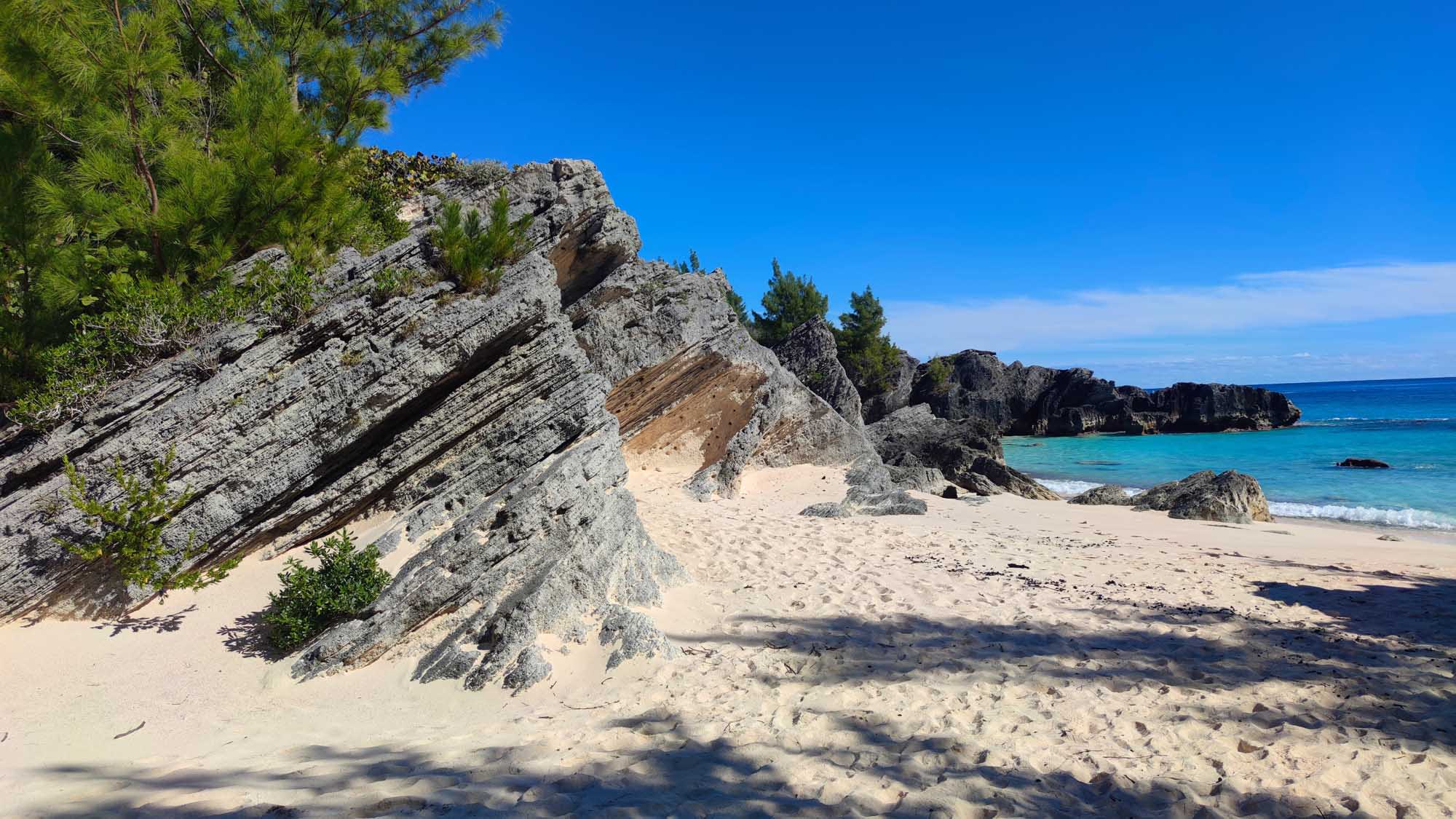 A pristine tropical beach in Bermuda featuring distinctive layered pink and gray rock formations