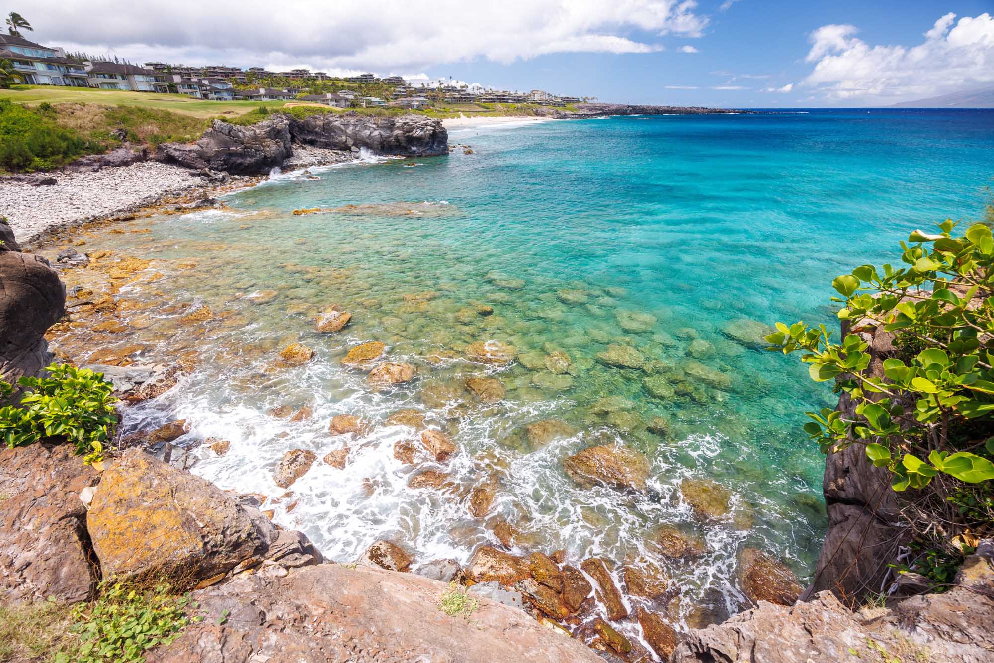 A stunning Hawaiian coastal landscape featuring crystal-clear turquoise waters, rocky outcrops