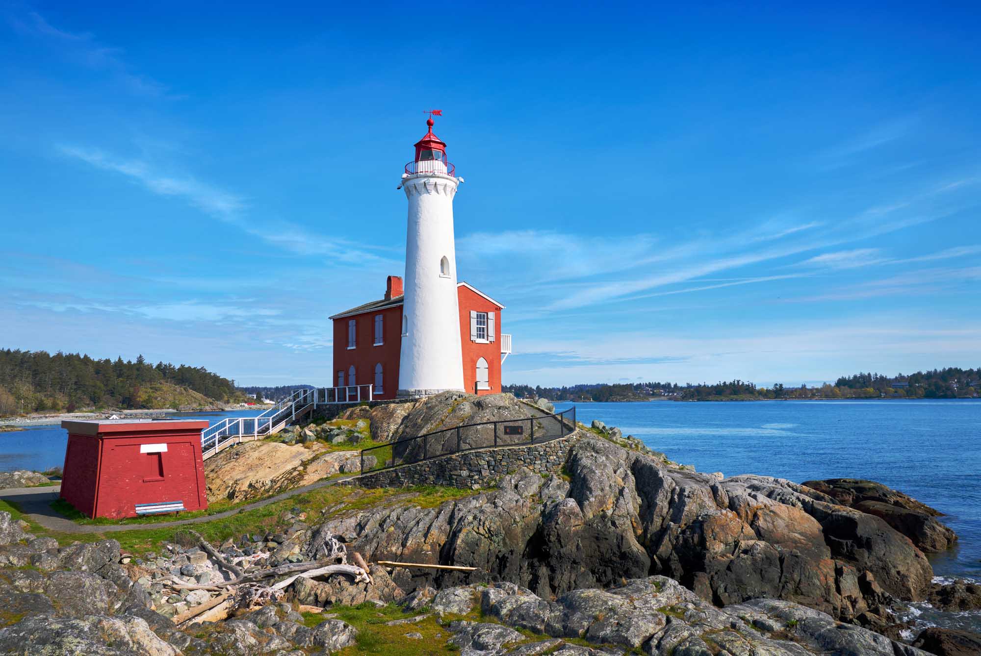 A historic red and white lighthouse situated on a rocky outcropping overlooking the Strait of Juan
