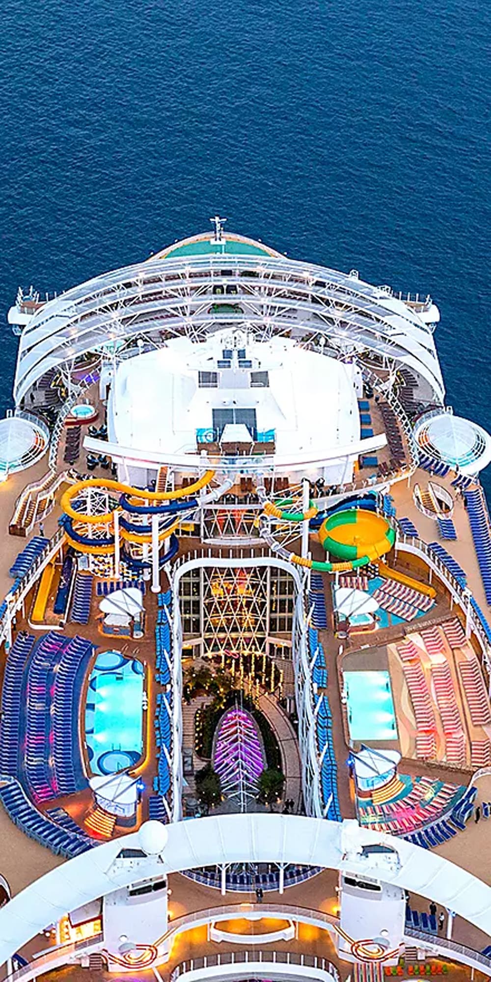 An overhead aerial view of a modern cruise ship's pool deck and upper areas, featuring colorful