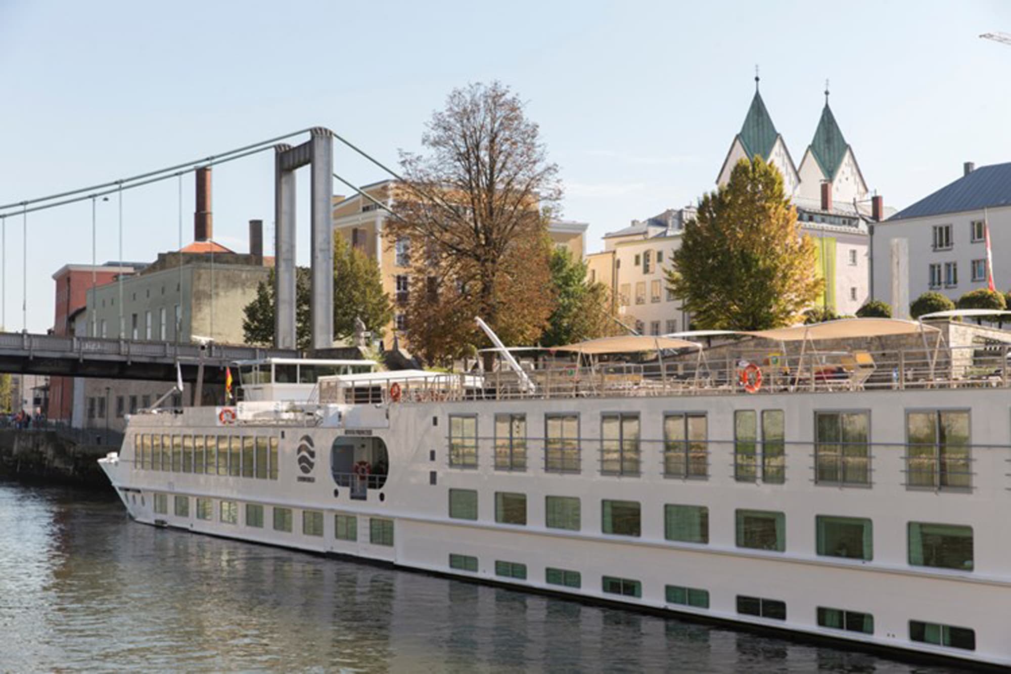 A modern river cruise ship with white hull and multiple passenger decks is moored alongside